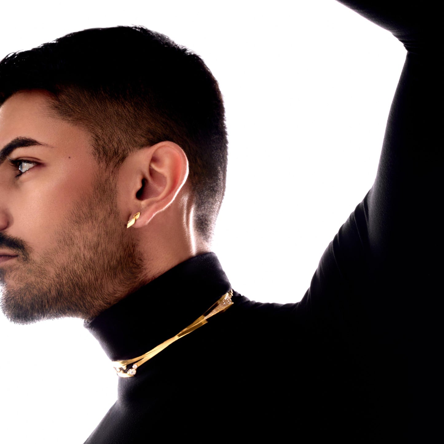 Man wearing a black turtleneck and gold necklace against a white background