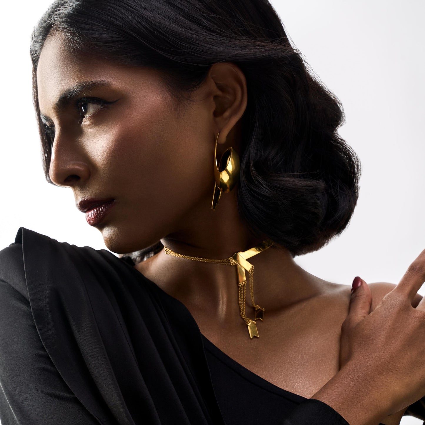 Woman wearing gold earrings with a black top against a white background
