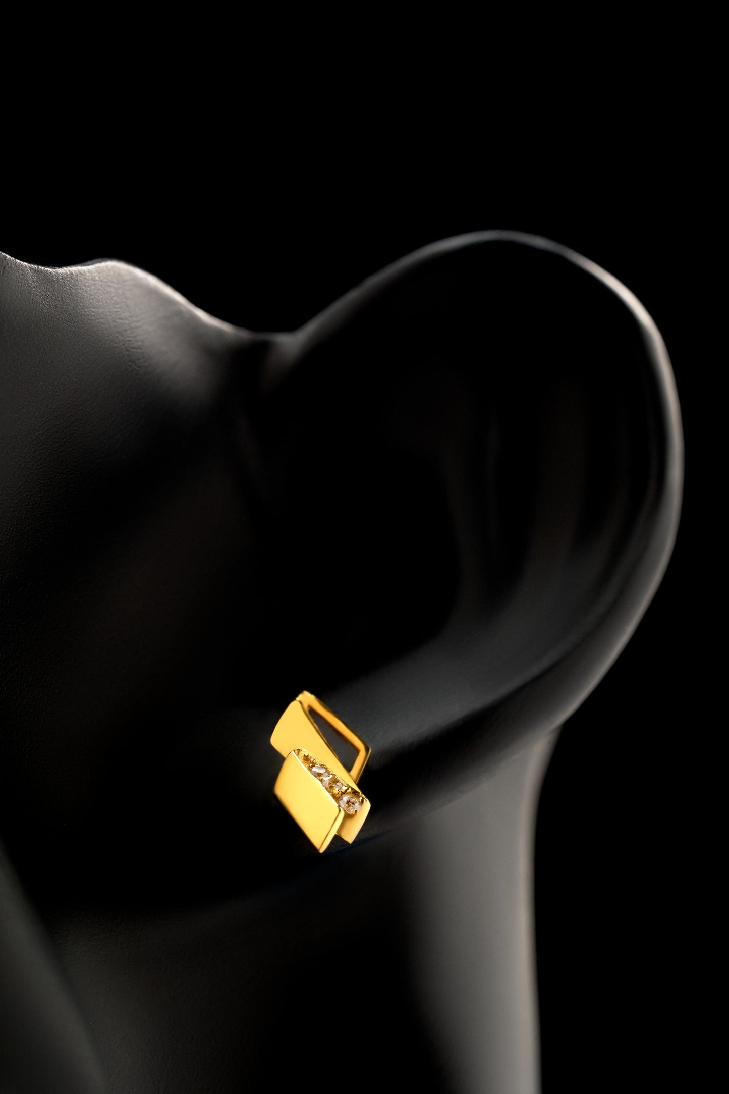 Gold earring on a black ear against a black background