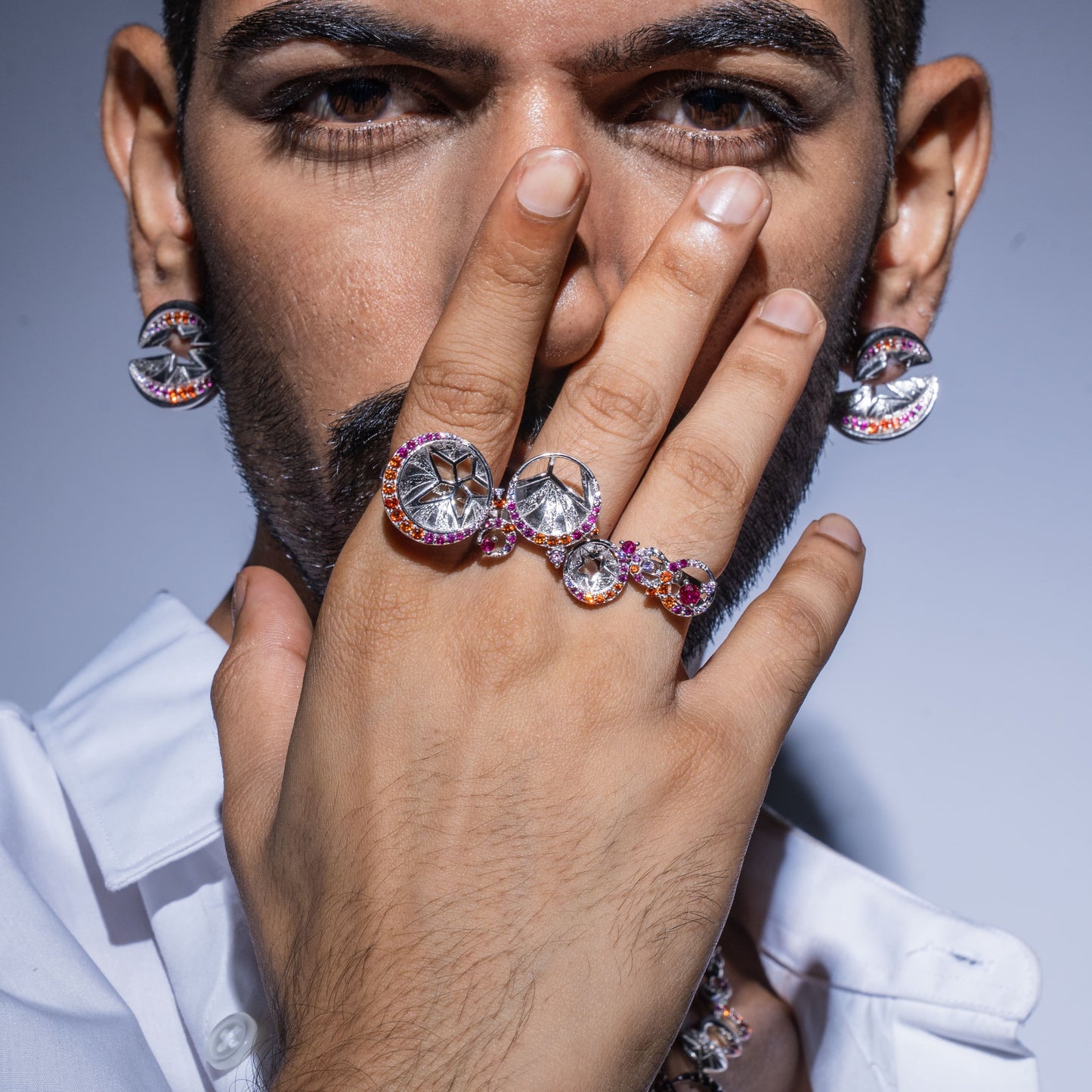 Man wearing a ring with multiple gemstones and earrings on a gray background