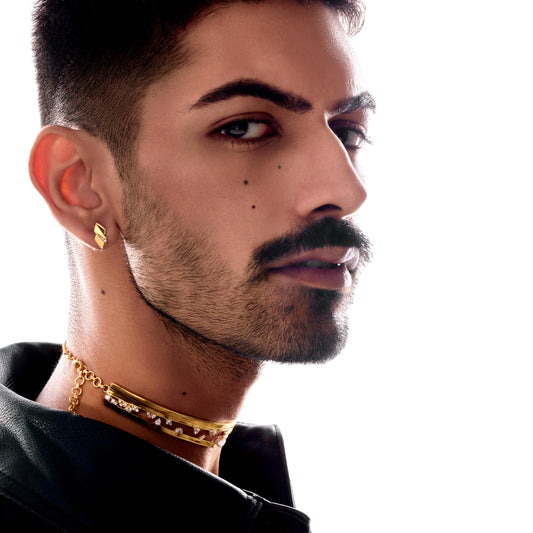 Man with styled hair and beard wearing a black jacket and gold jewelry on a white background