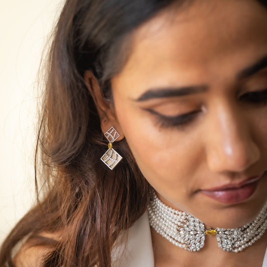 Woman wearing diamond earrings and a pearl necklace against a neutral background