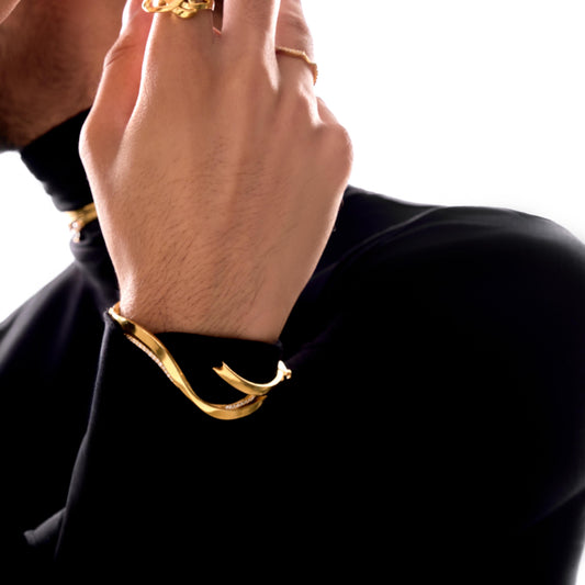 Hand wearing gold rings and bracelets on a black background